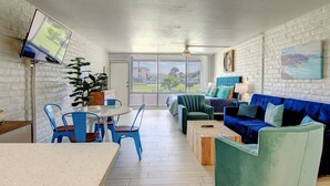 A modern living room with a blue sofa, green armchair, and a dining area with blue chairs.