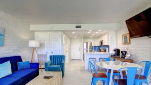 A modern kitchen with white cabinets, a stainless steel refrigerator, and a dining area with blue chairs and a white table.