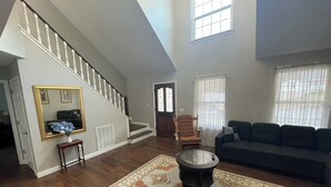 Un salón amplio con pisos de madera, un tapete grande, una chimenea, una escalera y un sofá de color oscuro.