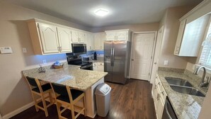 Una cocina con encimera de granito, armarios blancos, refrigerador de acero inoxidable y lavavajillas.