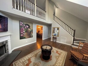 A spacious living room with a fireplace, a large rug, a coffee table, and a staircase leading to an upper level.