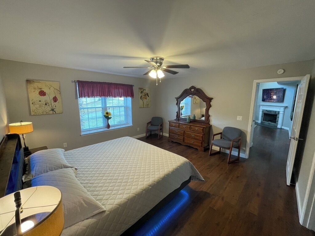 A bedroom with a bed, a ceiling fan, a dresser, a mirror, and a fireplace.
