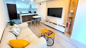 A modern living room with a sofa, coffee table, and TV. There is a dining area with chairs and a table, and a kitchen in the background. - Apartment in Barranco by Artline (Lima)