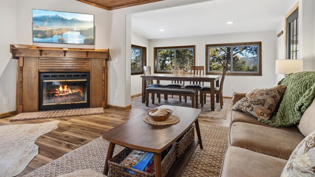 A cozy living room with a fireplace, a dining area, and large windows. - Mountain View Escape (Estes Park)