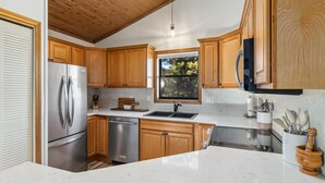 A modern kitchen with wooden cabinets, stainless steel appliances, a marble countertop, and a window providing a view of trees. - Mountain View Escape (Estes Park)
