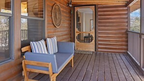 A wooden cabin with a wooden deck, a sofa with cushions, and a large window. - Mountain View Escape (Estes Park)