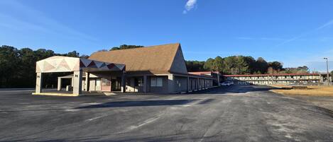 A motel with a central building and attached wings, featuring a parking lot and a clear sky.