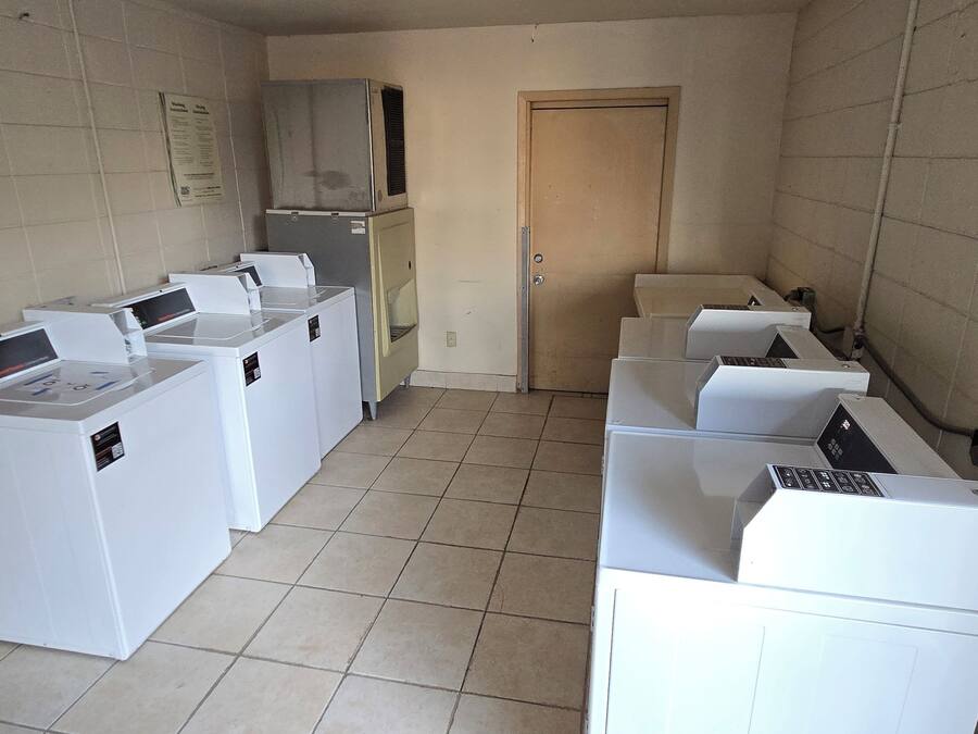 A laundry room with multiple washing machines and dryers, a tiled floor, and a door in the background.