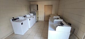 Un lavadero con varias lavadoras y secadoras, piso de baldosas y una puerta al fondo.