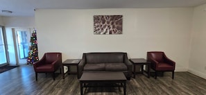Un salón con un sofá de cuero marrón oscuro, dos sillones a juego, una mesa de centro y una mesita auxiliar. Un cuadro grande de árboles adorna la pared.