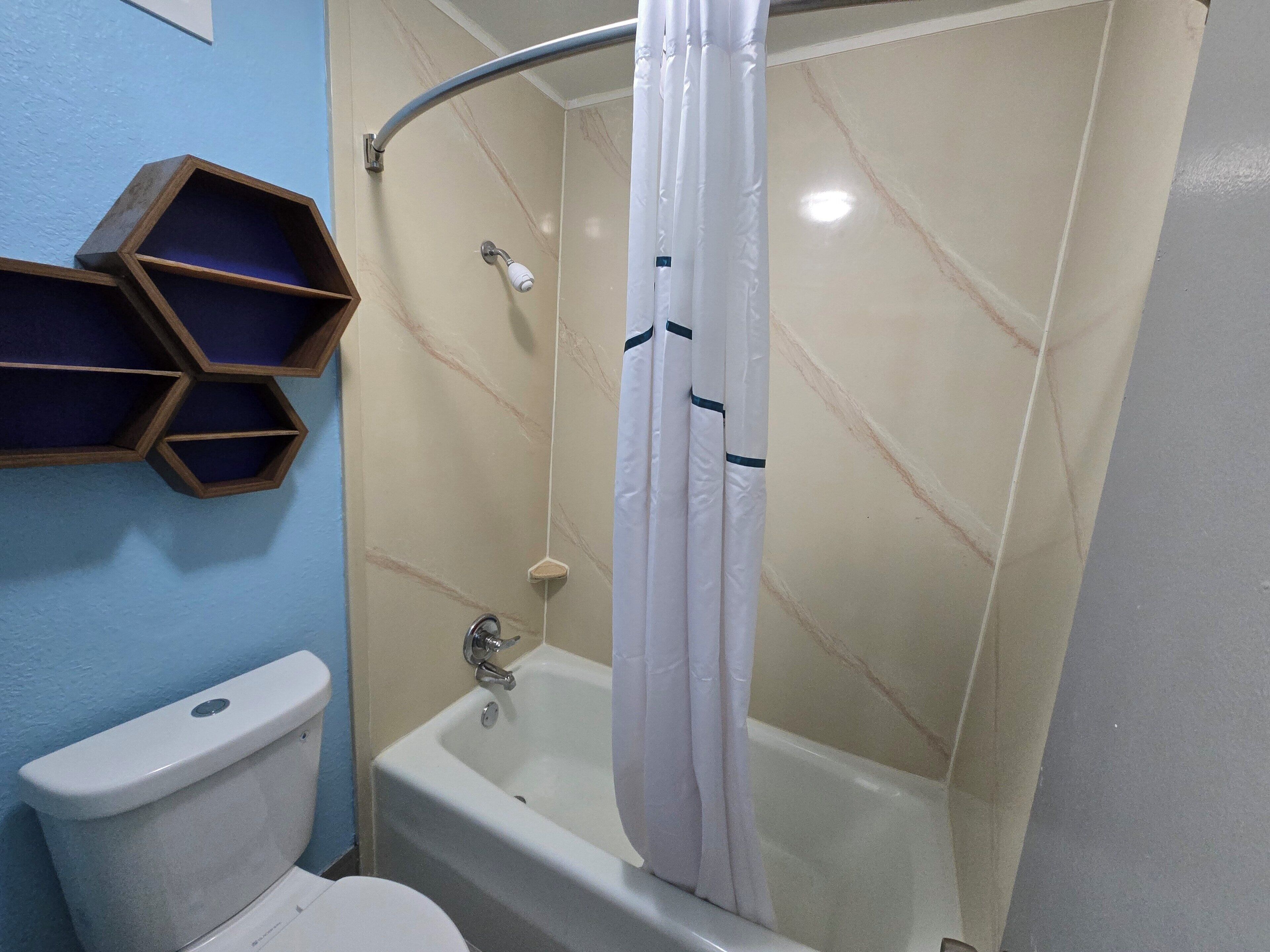 Un bagno con il water, una doccia con tenda bianca e un mobiletto a scaffali in legno.