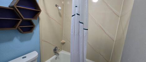 Un baño con inodoro, ducha con cortina blanca y estante de madera.