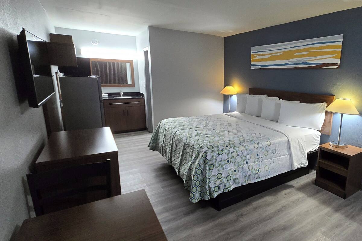 A hotel room with a bed, bedside tables, a TV mounted on the wall, and a painting above the bed.