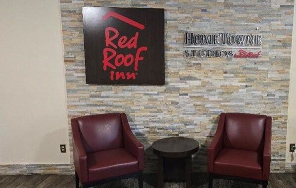 A Red Roof Inn sign and Home Town Studios sign on a stone wall. There are two leather chairs and a small round table. - HomeTowne Studios by Red Roof LaGrange (LaGrange)
