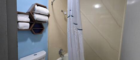 A bathroom with a toilet, a shower with a curtain, and a towel rack with multiple towels.