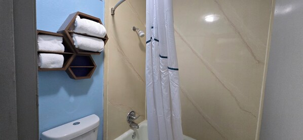 A bathroom with a toilet, a shower with a curtain, and a towel rack with multiple towels.