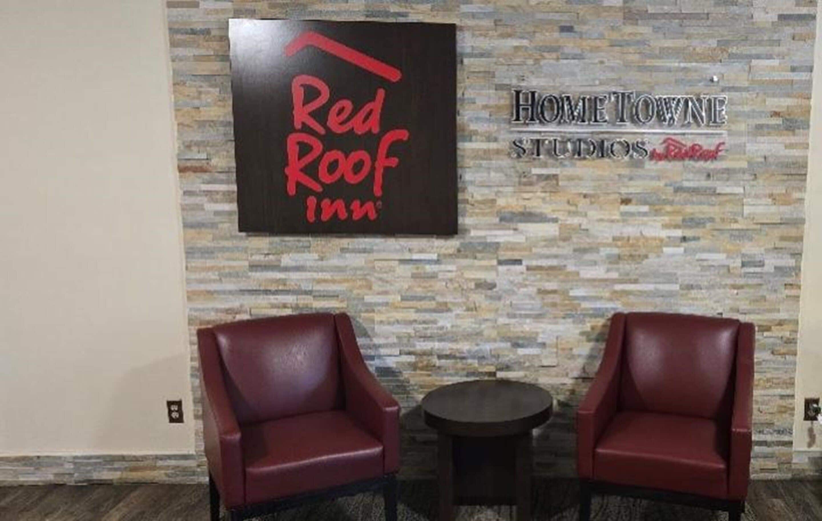 Se ven un letrero de Red Roof Inn y un letrero de Home Town Studios sobre una pared de piedra. Hay dos sillones de cuero y una pequeña mesa redonda.
