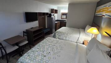 Habitación de hotel con dos camas, un escritorio, una silla, un televisor, kitchenette y un cuadro en la pared.