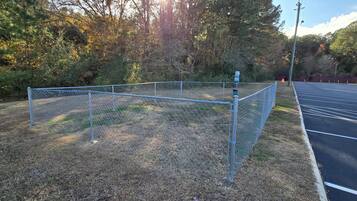 Ein von einer Hecke umgebener Parkplatz mit Sportplatz, umgeben von Bäumen und einem Gebäude im Hintergrund.
