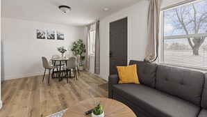 En moderne stue med en grå sofa, et rundt sofabord med en plante, og et spiseområde med bord og stole.