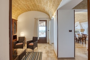 A spacious hallway with a high ceiling, a dining area with wooden furniture, and a view through a door to an outdoor patio.
