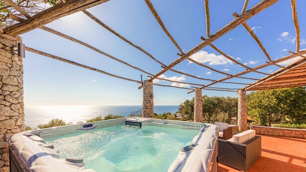 Un bain à remous avec un mur en pierre d’un côté et une pergola avec des poutres en bois.