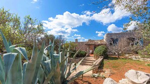 Un bâtiment en pierre avec un toit en tuiles, entouré de plantes d’agave et d’un jardin agrémenté d’un sentier en pierre.
