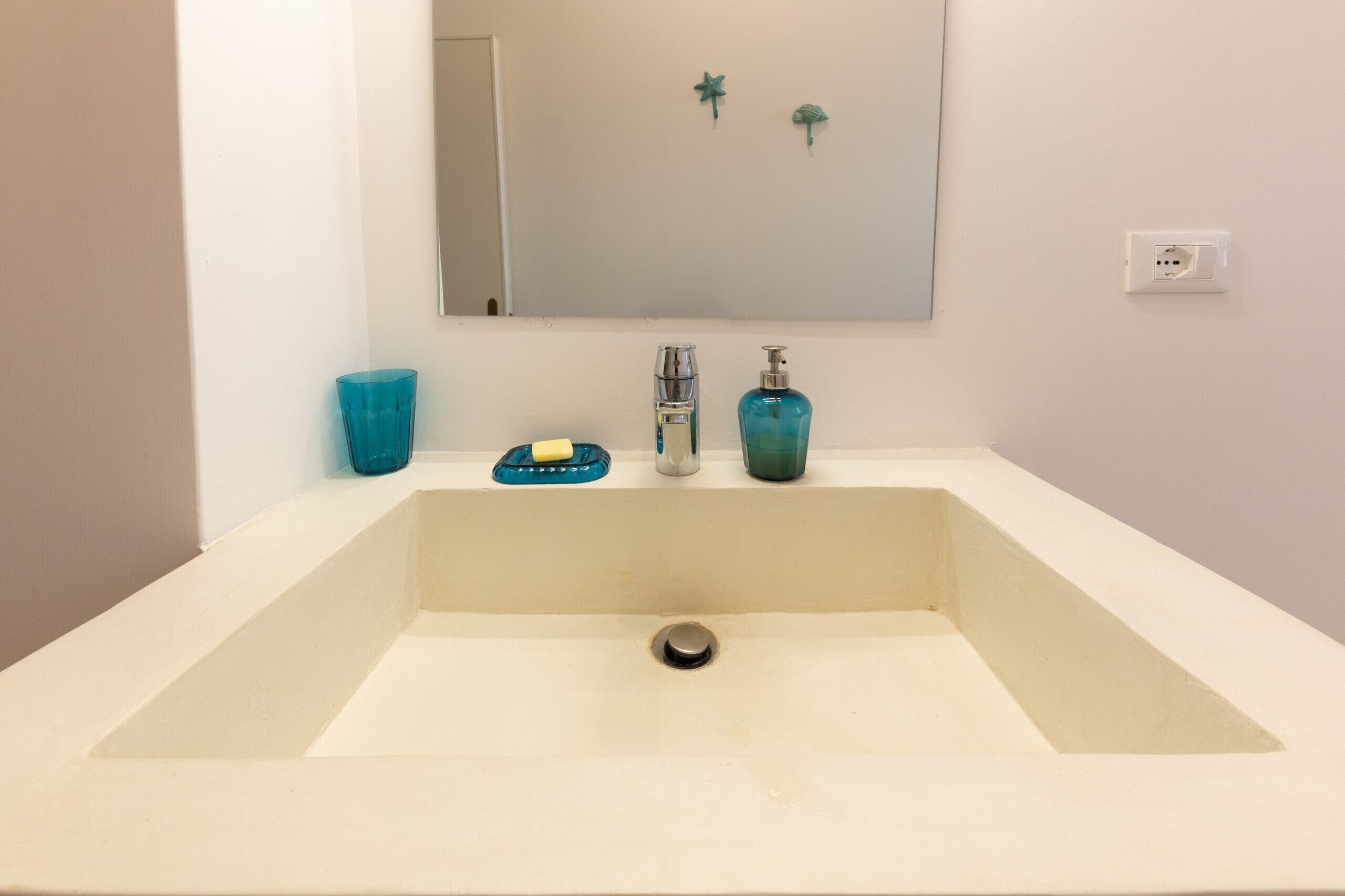 A bathroom sink with a mirror above it, a blue soap dish, and a blue soap dispenser.