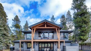 A modern two-story house with a wooden deck and large windows. - Sleeps 16+ | 7 bed 7.5 bath | EV | Hot tub | SHARC (Sunriver)