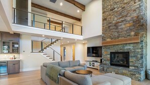 A spacious living area with a stone fireplace, a large gray sectional sofa, a wooden coffee table, and a staircase leading to an upper level. - Sleeps 16+ | 7 bed 7.5 bath | EV | Hot tub | SHARC (Sunriver)
