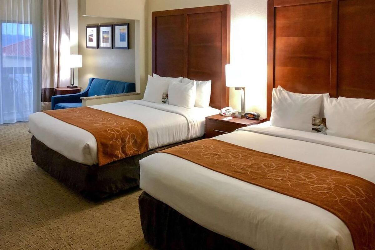 Een hotelkamer met twee bedden, een bureau, een stoel en een groot raam met gordijnen.