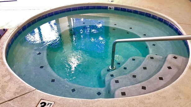 Un jacuzzi con borde de azulejos y escalera metálica.