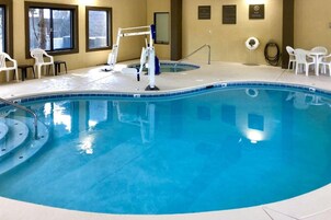 An indoor swimming pool with a diving board, lounge chairs, and safety signs.