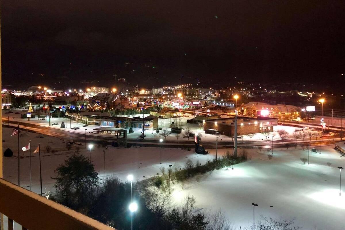 Een nachtzicht van een stad met verlichte gebouwen en een parkeerplaats bedekt met sneeuw.
