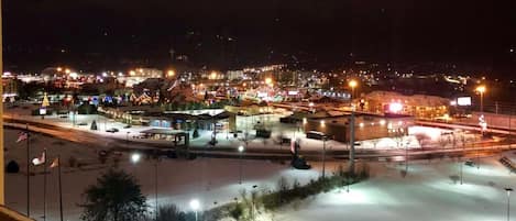 A nighttime view of a town with illuminated buildings and a snow-covered parking lot.