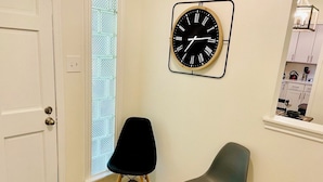 Une pièce avec une porte blanche, une chaise noire et grise, un plancher en bois et une horloge fixée au mur.