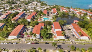 Vista aérea de un complejo turístico costero con varias edificaciones, piscina y puerto deportivo.