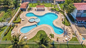 Vista aérea de un complejo turístico con una piscina central, varias edificaciones para huéspedes y palmeras circundantes.