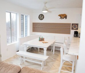 Een eethoek met een witte tafel en banken, een plafondventilator en een klok aan de muur.