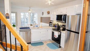 A modern kitchen with white cabinets, stainless steel appliances, and a herringbone wood floor.