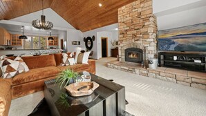 Un salon spacieux doté d’une cheminée en pierre, d’un grand téléviseur à écran plat et d’un coin salon confortable avec un canapé marron et une table basse.