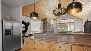 Une cuisine moderne dotée de meubles en bois, de plans de travail en granit, d’appareils électroménagers en acier inoxydable et d’une cheminée en pierre.