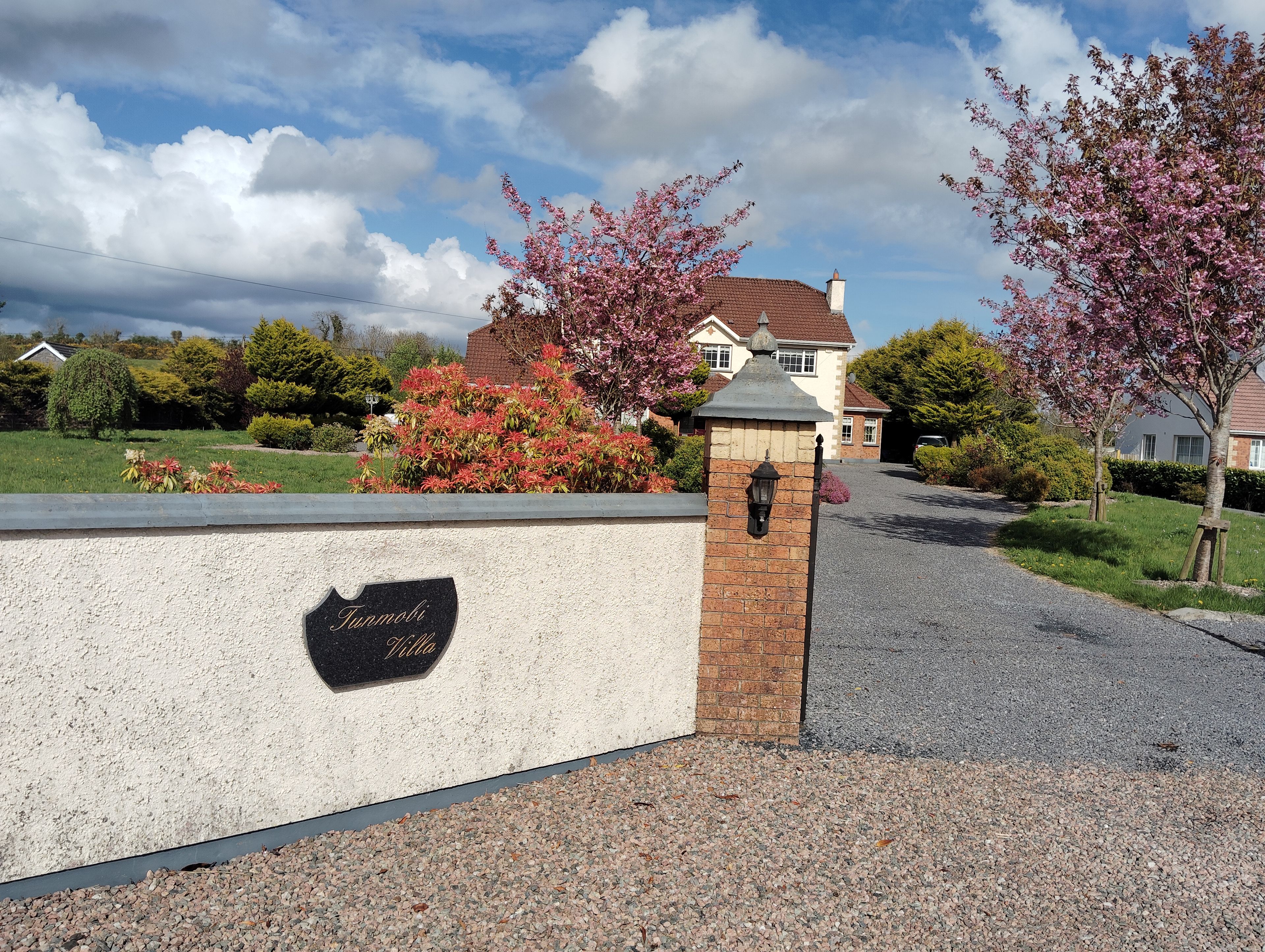 A gated entrance with a sign reading 'Farnoli Villa' and a gravel driveway leading to a house with a red roof.