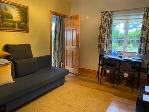 A living room with a sofa, a dining table with chairs, a door, and a window with curtains. - Welcome to Tunmobi Villa, home away from home.

 (Ballyjamesduff)
