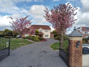 A residential driveway leading to a house with a gravel path, surrounded by flowering trees and a gated entrance. - Welcome to Tunmobi Villa, home away from home.

 (Ballyjamesduff)
