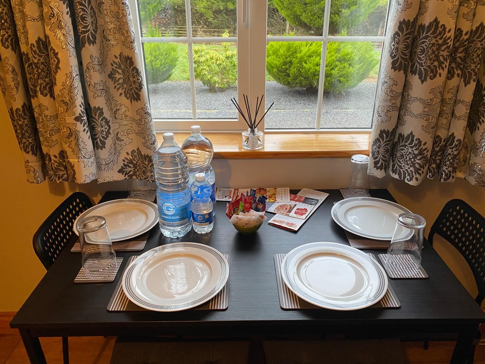 A dining table set for four with water bottles, a menu, and a decorative bowl.