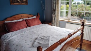 A bedroom with a wooden bed, a painting on the wall, a window with a view of greenery, and a radiator. - Welcome to Tunmobi Villa, home away from home.

 (Ballyjamesduff)