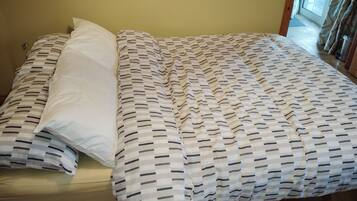 A bed with a patterned bedspread and pillows, a wooden floor, and a door leading to a hallway.