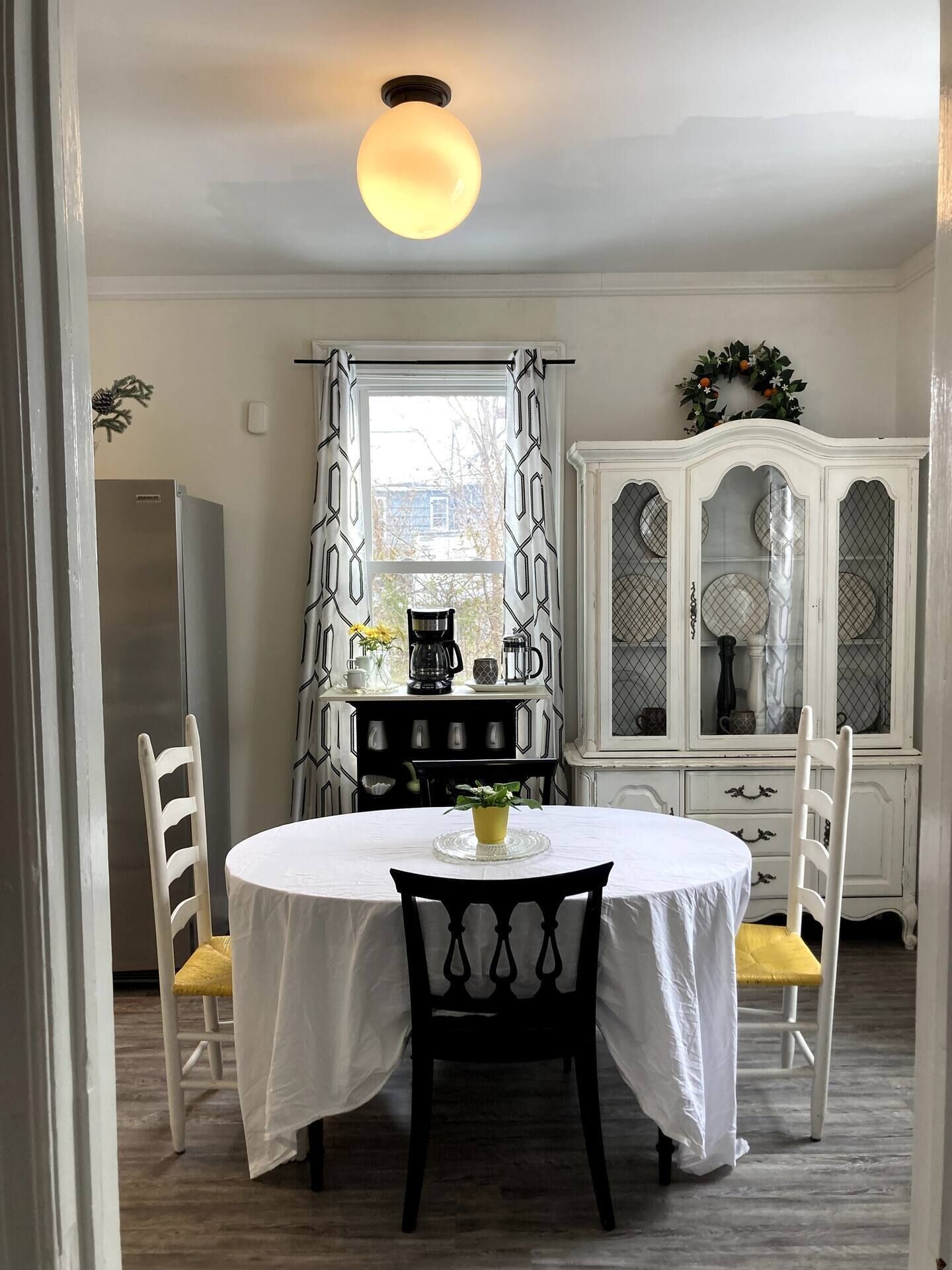 A dining area with a round table, two chairs, a white cabinet with glass doors, and a ceiling light fixture.
