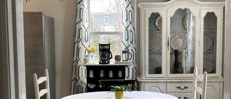 A dining area with a round table, two chairs, a white cabinet with glass doors, and a ceiling light fixture.